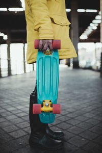 Young woman in yellow coat prepares and uses her electric skateboard.