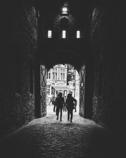 Rear view of people walking on alley amidst buildings in city