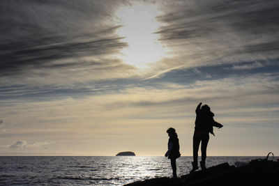 Silhouette men standing on beach against sky during sunset