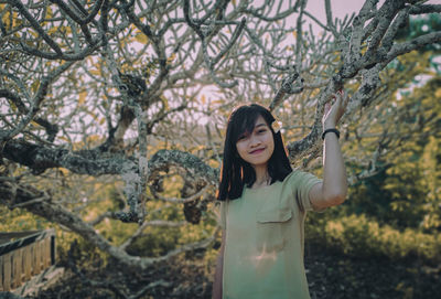 Portrait of young woman standing by tree