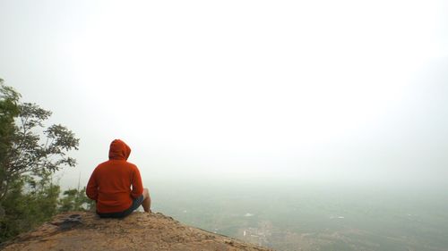 Man sitting on rock against sky during foggy weather