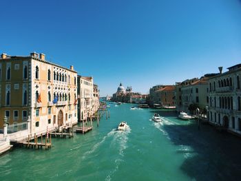 Boats in canal amidst buildings against clear blue sky