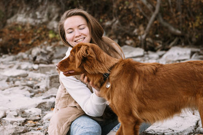 Young woman and dog retriever walks on river shore at autumn season