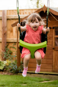 Full length of happy girl swinging at backyard