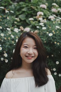 Portrait of smiling young woman standing against flowers park