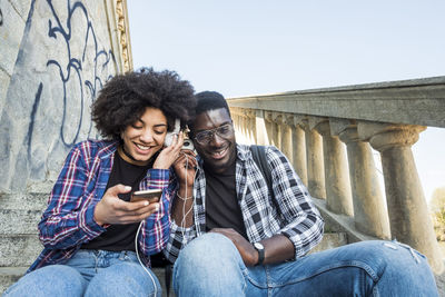 Low angle view of man and woman listening music on headphones while sitting on steps 