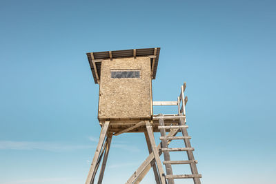 Low angle view of raised hide against clear blue sky