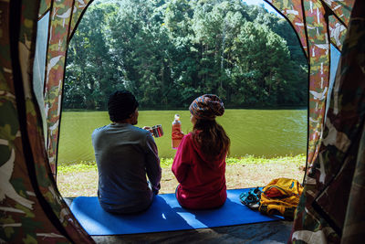 Rear view of people sitting on mat by lake