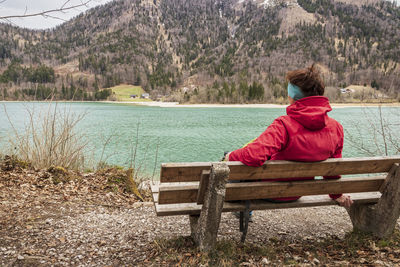 Rear view of woman sitting on bench by lake