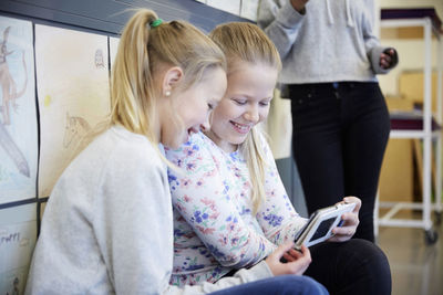 Smiling middle school girls using mobile phone in corridor