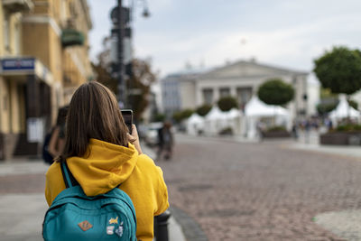 Rear view of woman photographing on footpath against buildings