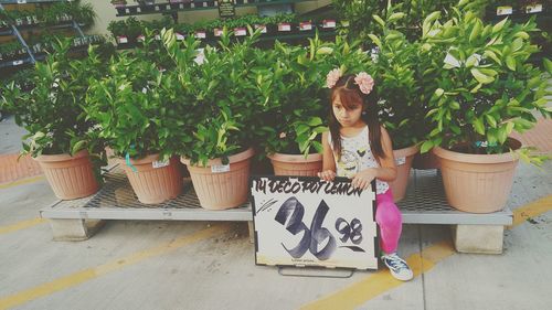 Girl holding price tag while sitting by potted plants