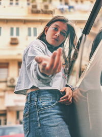 Low angle portrait of young woman gesturing while standing against building in city