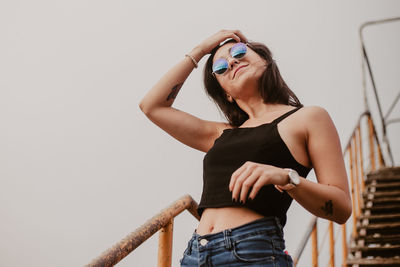 Young woman in sunglasses standing against clear sky