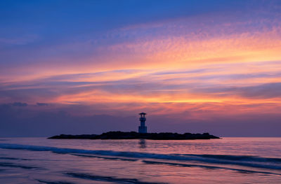 Lighthouse by sea against sky during sunset
