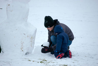 Father and son making snowman during snowfall