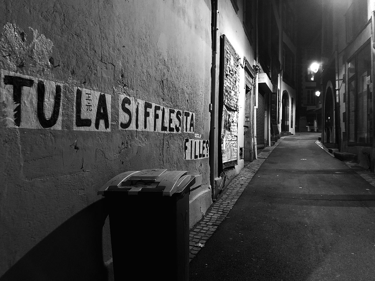 black, road, darkness, architecture, street, alley, black and white, white, built structure, text, infrastructure, monochrome, monochrome photography, western script, communication, building exterior, city, light, no people, the way forward, wall - building feature, lane, sign, illuminated, night, building, graffiti, urban area, snapshot, transportation, footpath, lighting equipment, outdoors