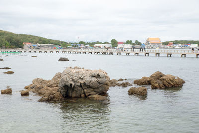 Rocks on sea by buildings against sky