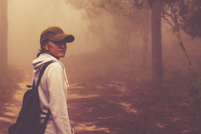 Side view portrait of young woman standing in forest during foggy weather