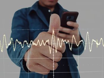 Digital composite image of graph and man using smart phone against white background