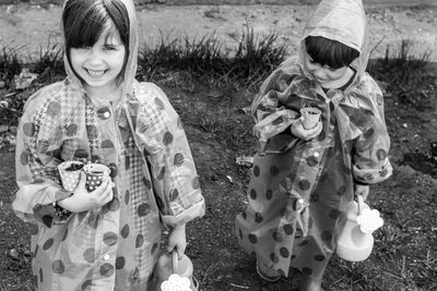 Portrait of smiling siblings in raincoat sanding outdoors