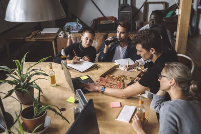 High angle view of colleagues eating pizza while working at workplace