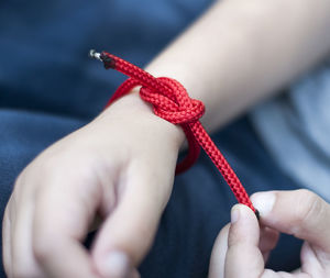 Close-up of hand tying knot with red string on hand