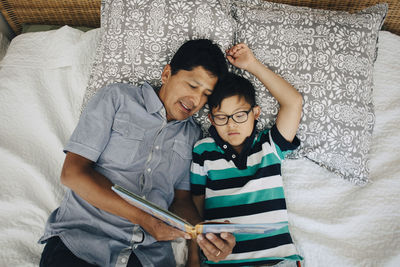 High angle view of father reading book to son while lying on bed at home