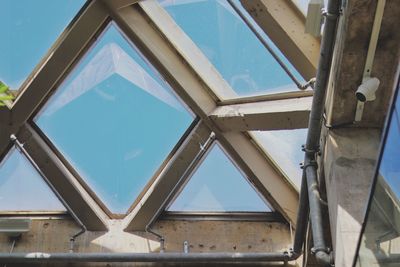 A security camera surveys below a concrete and glass ceiling against a blue sky