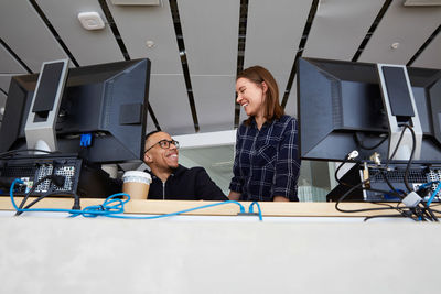 Low angle view of smiling friends talking while using computers at university