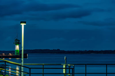 Illuminated railing by sea against sky at dusk