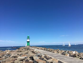 Lighthouse by sea against clear blue sky