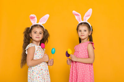 Portrait of happy friends holding heart shape against yellow background