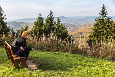 Side view of man sitting on seat against trees