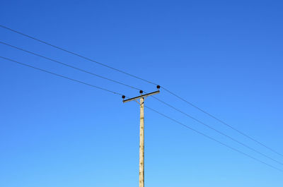 Low angle view of electricity pylon against blue sky