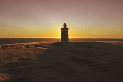 Lighthouse by sea against sky during sunset