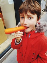 Close-up portrait of cute boy eating carrot while standing outdoors