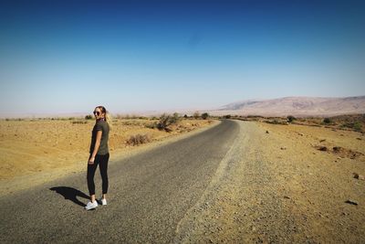 Portrait of mid adult woman standing on road against clear blue sky