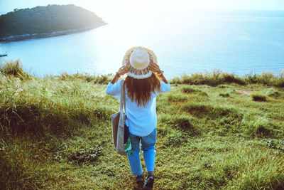 Rear view of woman walking on field by sea against sky