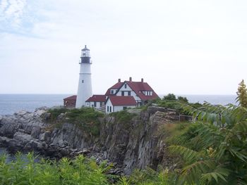 Lighthouse amidst sea and buildings against sky