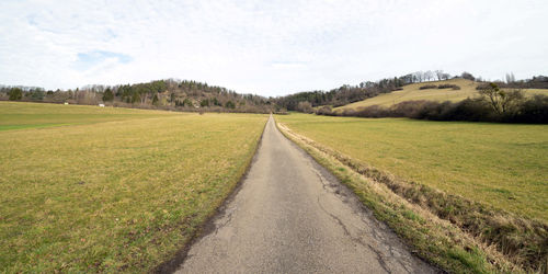 Dirt road amidst field against sky