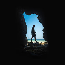 Man with camera standing by cave against sea and sky