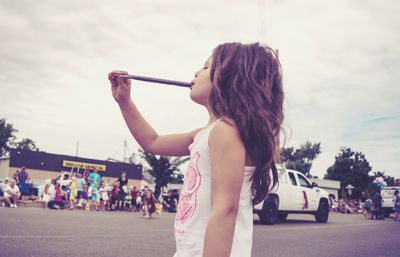 Girl eating popsicle while standing on street against sky