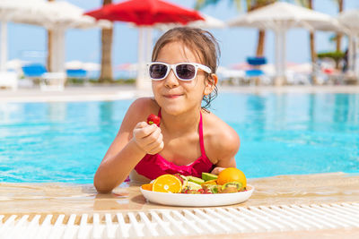 Smiling girl eating strawberry at poolside