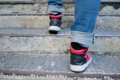 Close-up of a pair of legs walking up some stairs, wearing a pair of jeans and casual red sneakers