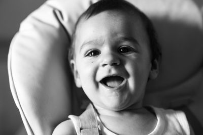 Close-up portrait of cute baby boy laughing while lying in stroller at home