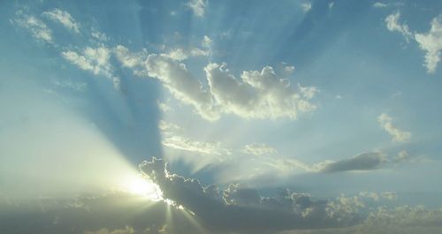 Low angle view of sunlight streaming through clouds