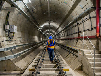 Full length of worker walking on railroad track in tunnel