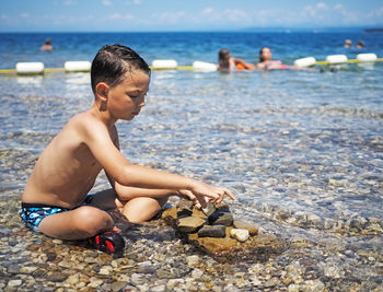 Full length of shirtless boy playing with stones on shore at beach