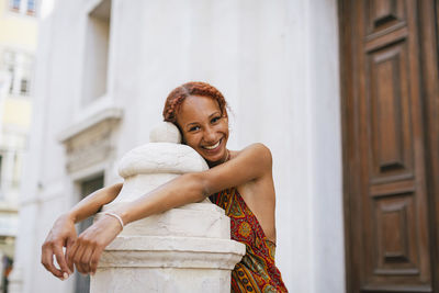 Happy young woman with curly hair leaning on bollard